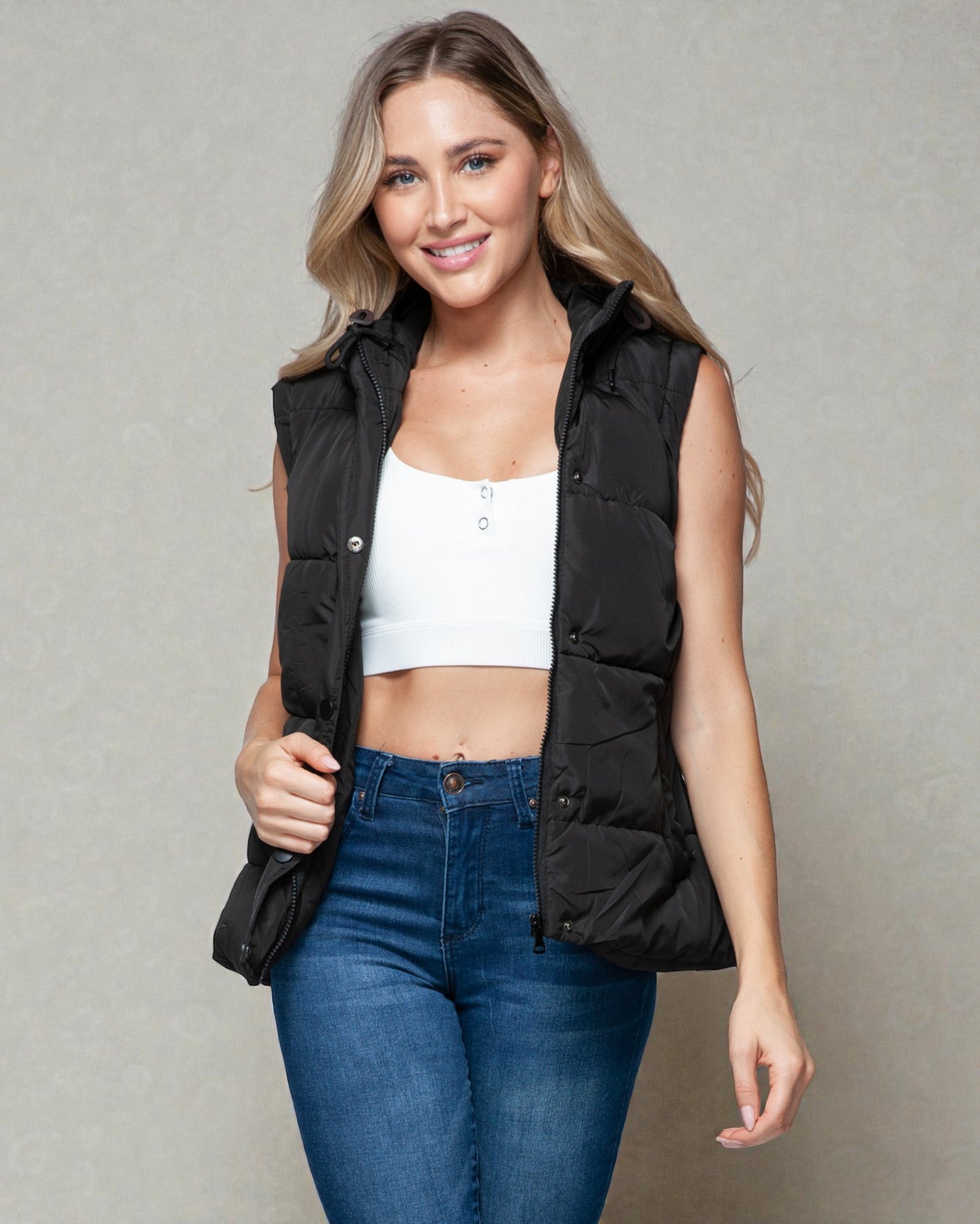 Woman wearing a black vest over a white top and blue jeans on a gray background