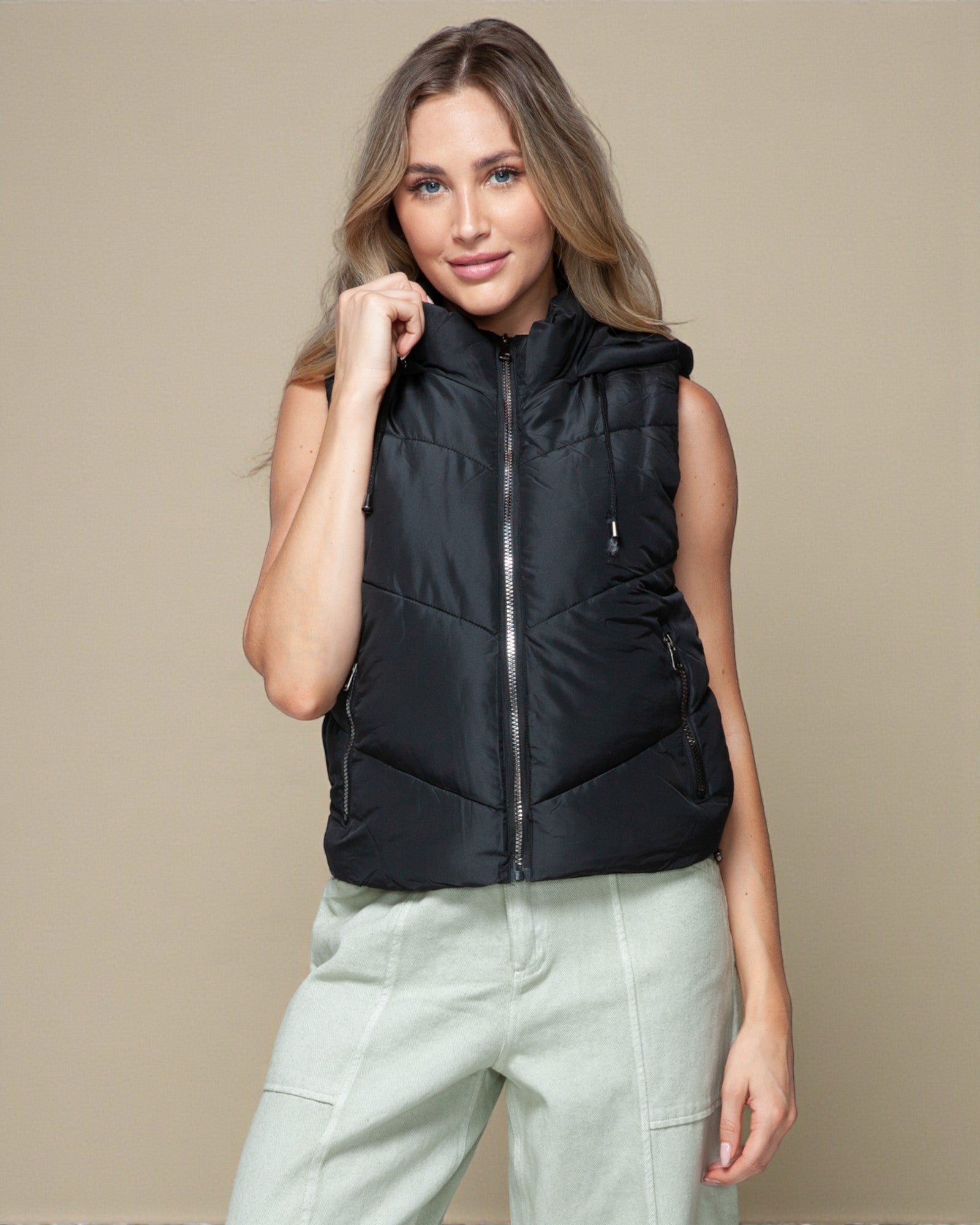 Woman wearing a black puffer vest against a beige background