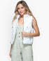 A woman modeling a sleeveless white puffer vest over a sage green jumpsuit, photographed against a clean white studio background.