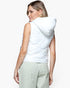 A woman shown from the back wearing a sleeveless white puffer vest with an attached hood and light sage green pants, against a plain light gray studio background.