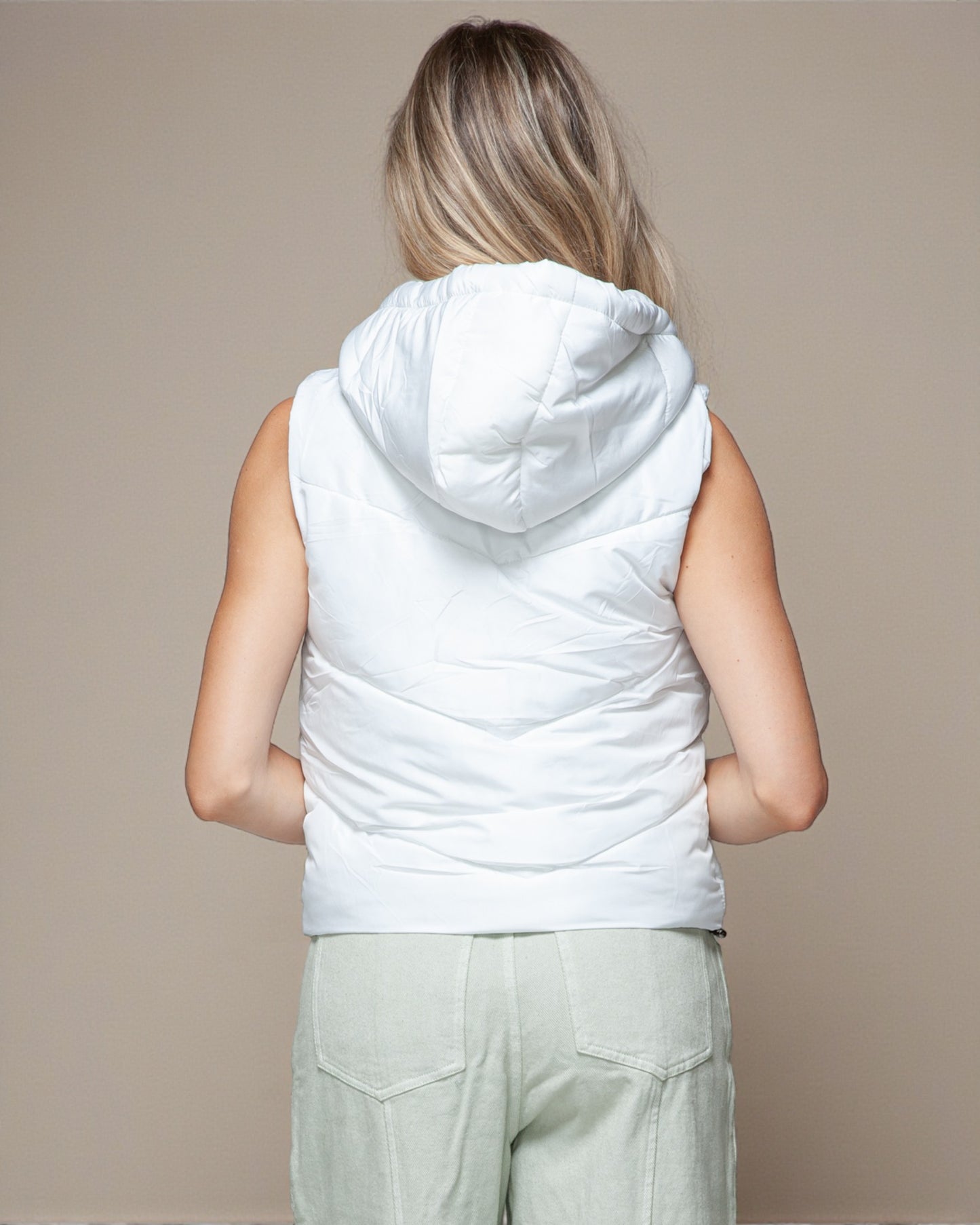 Person wearing a white sleeveless hooded jacket against a beige background