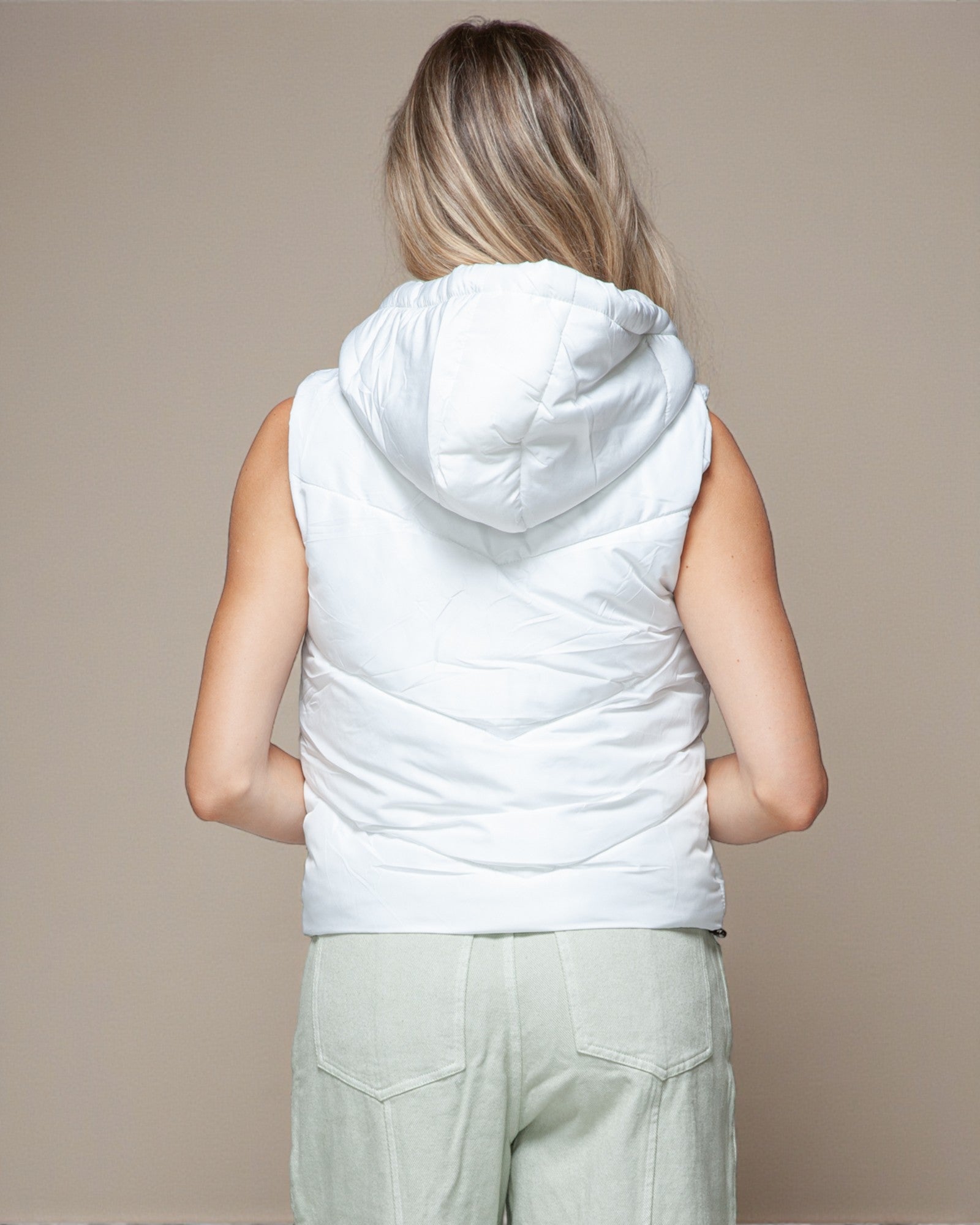 Person wearing a white sleeveless hooded jacket against a beige background