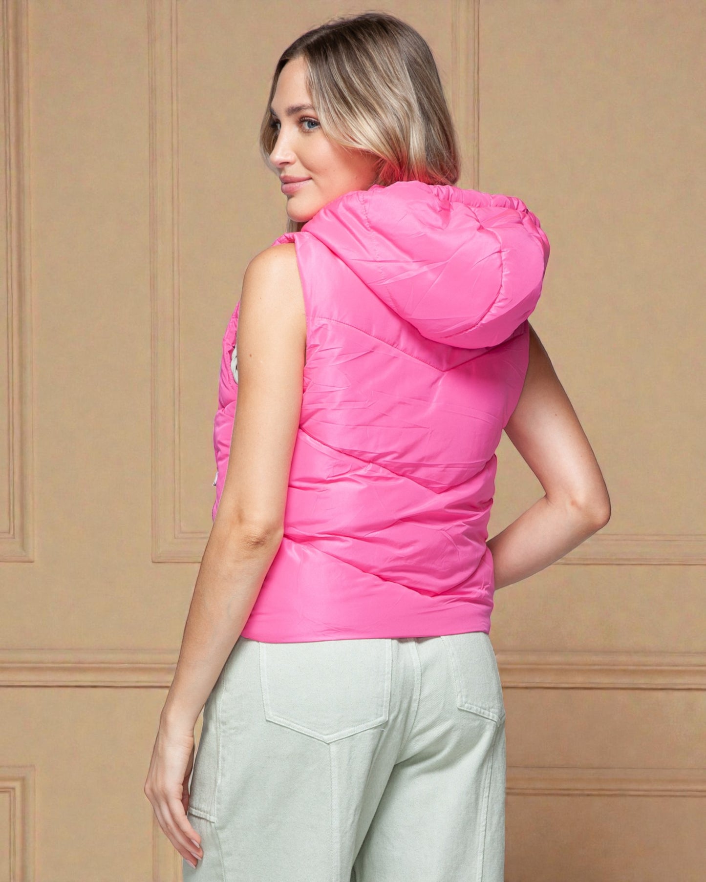 Woman wearing a pink puffer vest against a beige wall