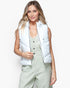 A woman modeling a sleeveless white puffer vest over a sage green jumpsuit, photographed against a clean white studio background.