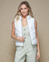 Woman wearing a white puffer vest over a light green jumpsuit against a beige background
