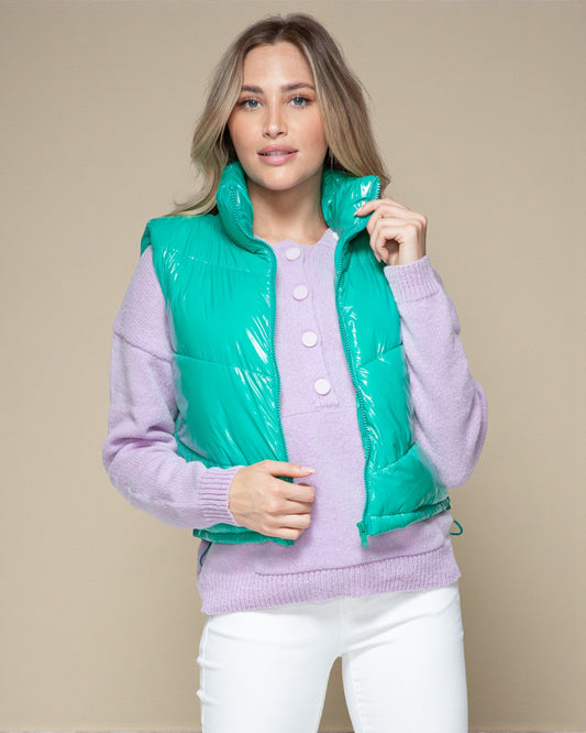 Woman wearing a purple sweater with a green puffer vest against a beige background