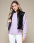 Woman wearing a purple sweater and black puffer vest on a beige background