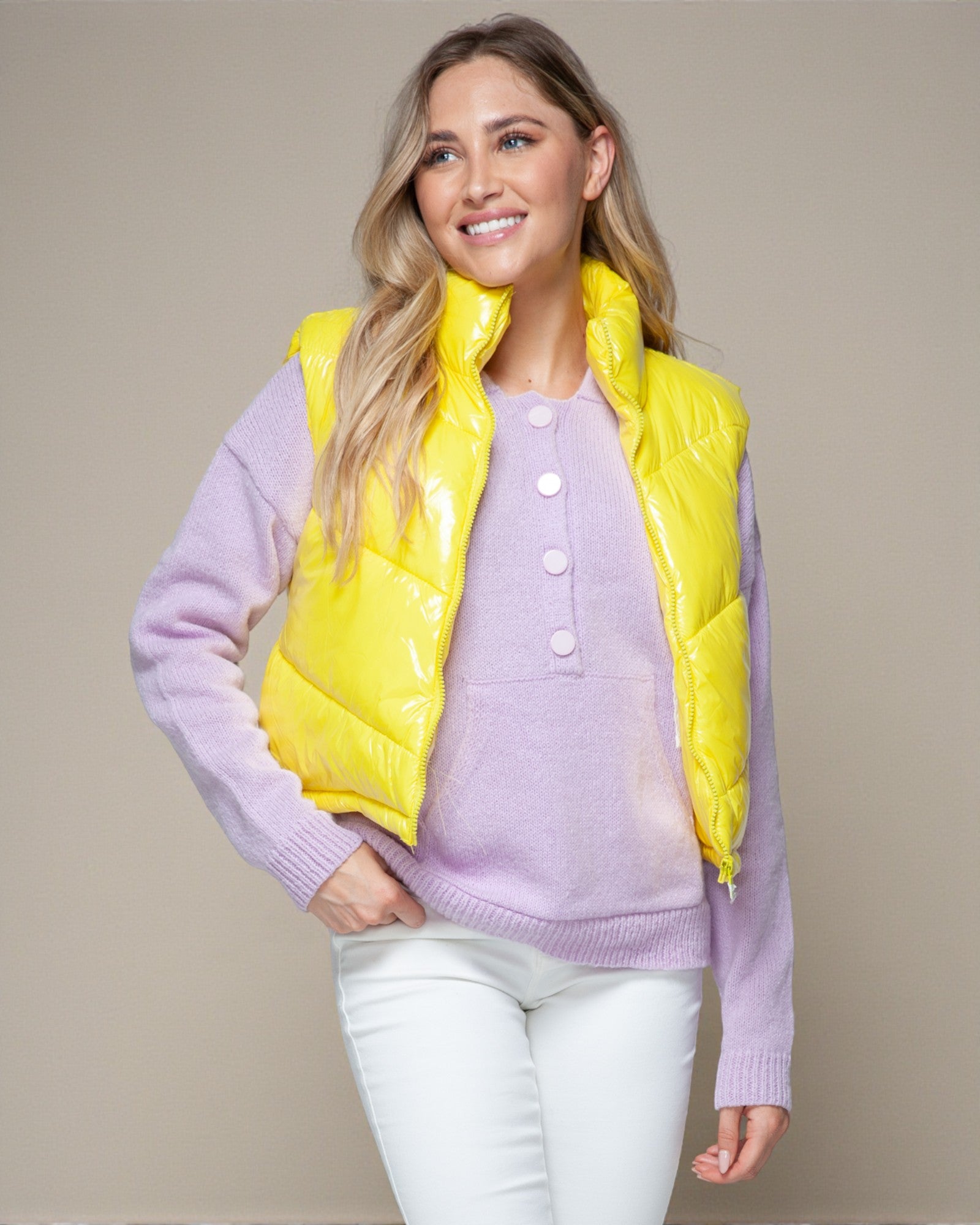Woman wearing a yellow puffer vest over a purple sweater on a beige background
