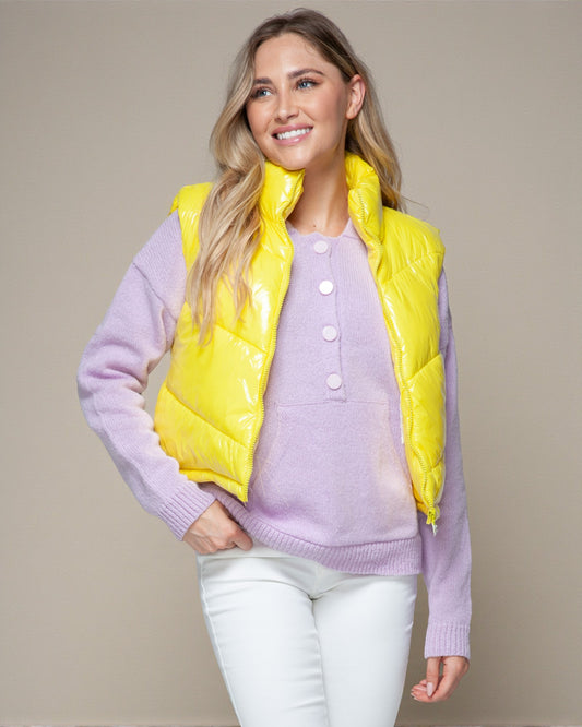 Woman wearing a yellow puffer vest over a purple sweater on a beige background