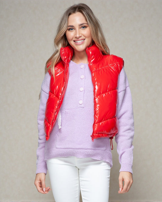 Woman wearing a red puffer vest over a light purple sweater on a neutral background