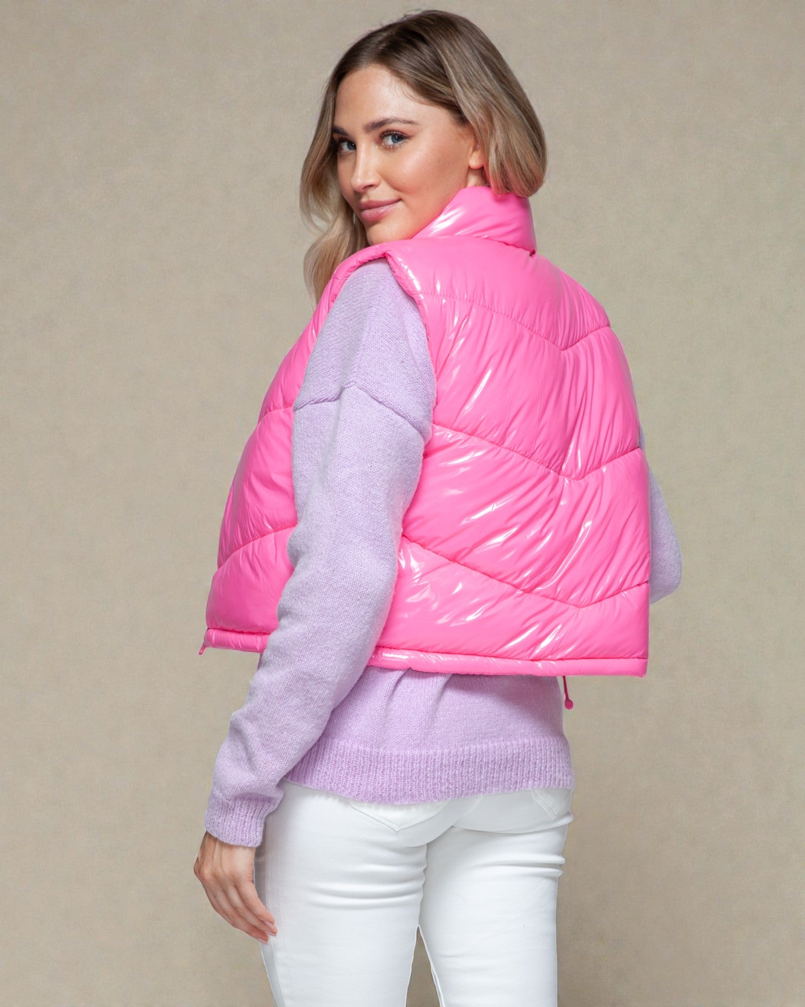 Woman wearing a pink puffer vest over a purple sweater on a beige background