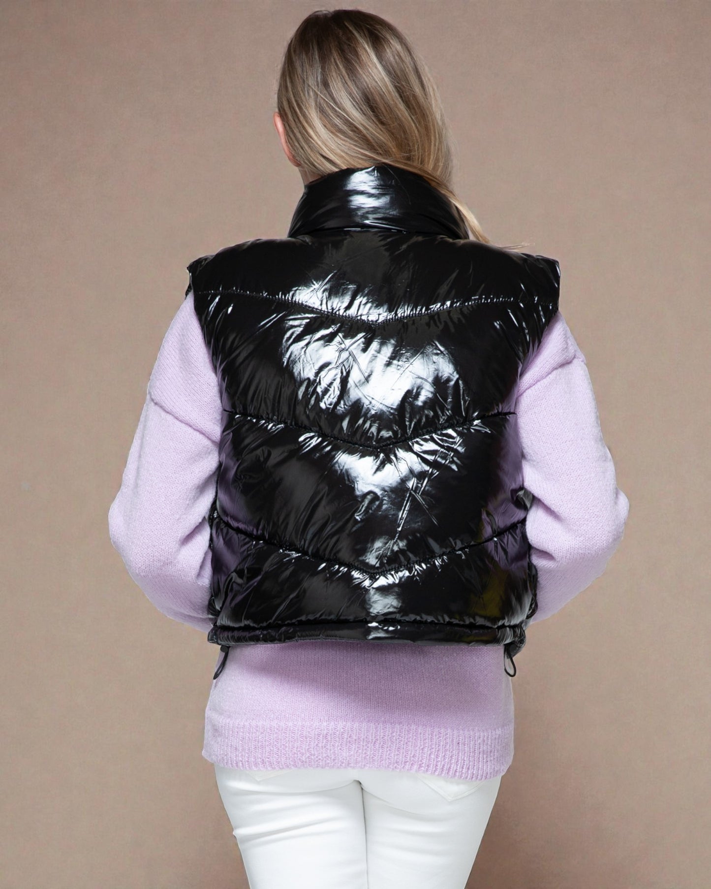 Person wearing a black puffer vest over a pink sweater on a beige background