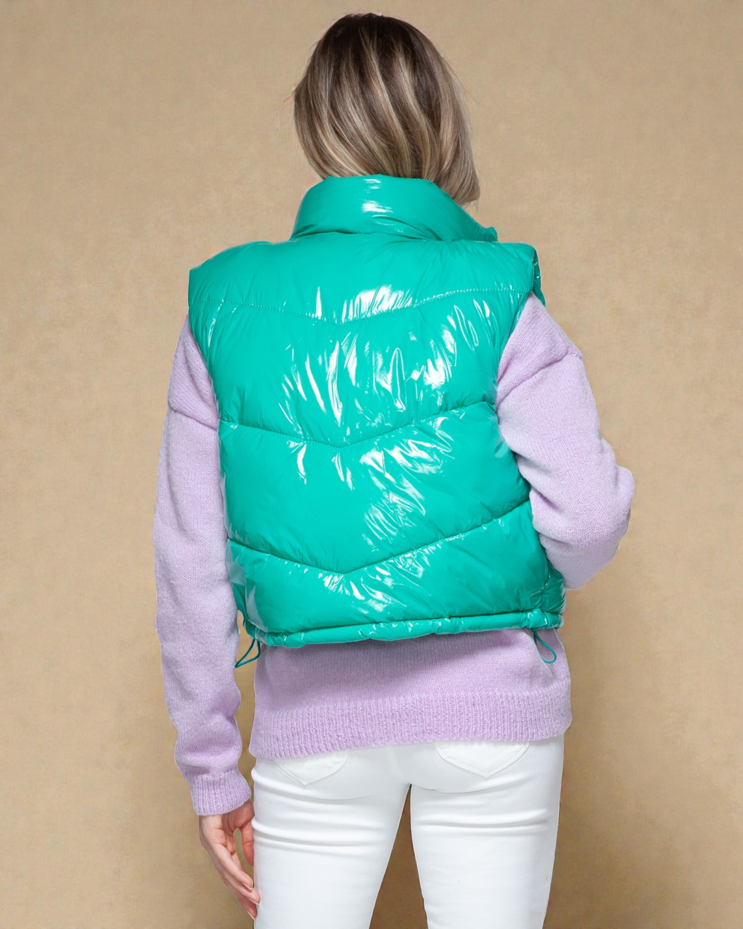 Person wearing a teal puffer vest over a light purple sweater on a beige background