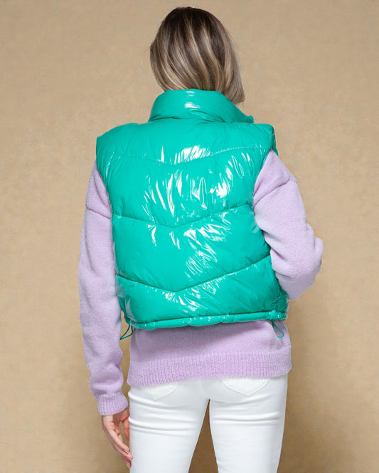 Person wearing a teal puffer vest over a light purple sweater on a beige background