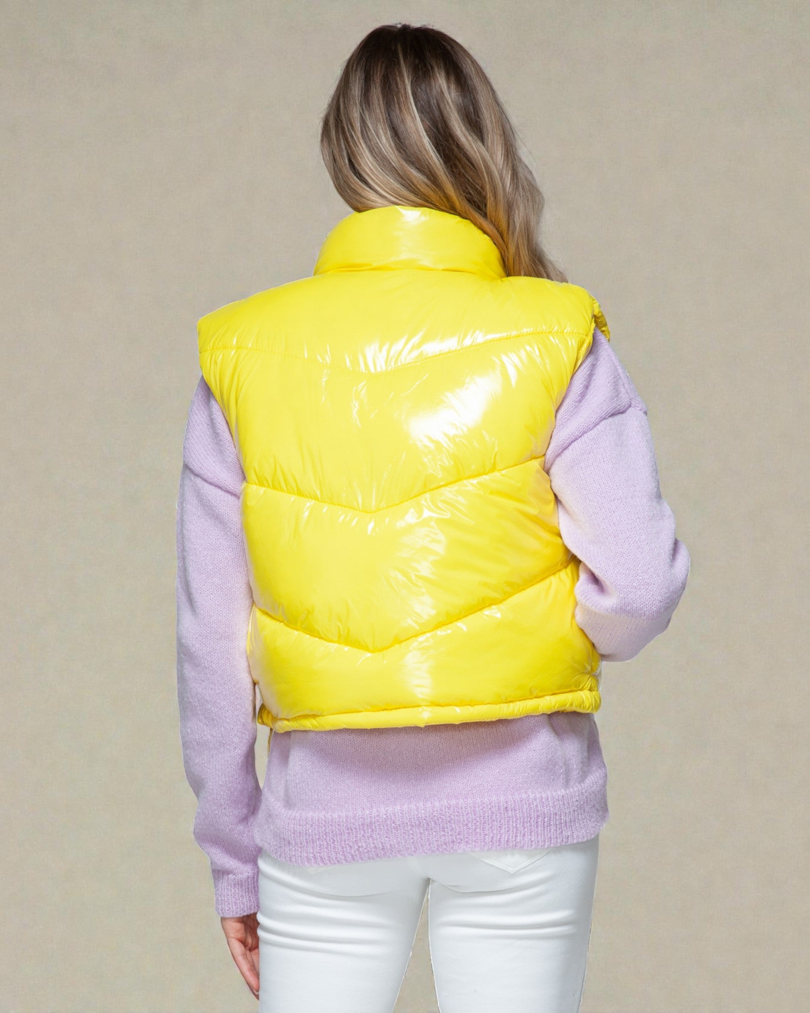 Person wearing a yellow puffer vest over a light purple sweater on a beige background