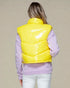 Person wearing a yellow puffer vest over a light purple sweater on a beige background