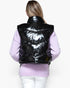 A woman viewed from behind wearing a shiny black puffer vest over a light purple sweater and white pants, against a plain light background.