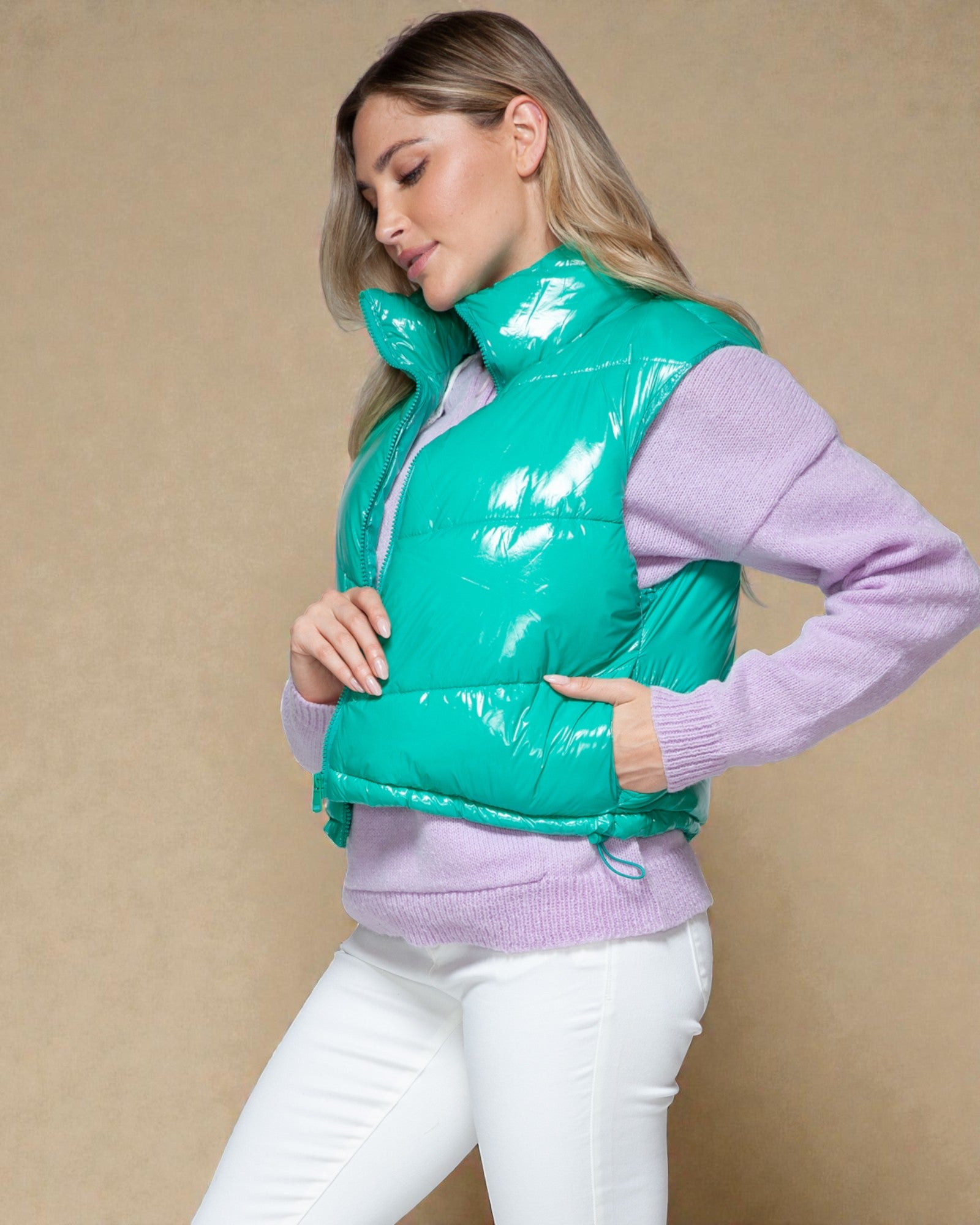 Woman wearing a green puffer vest over a purple sweater on a beige background