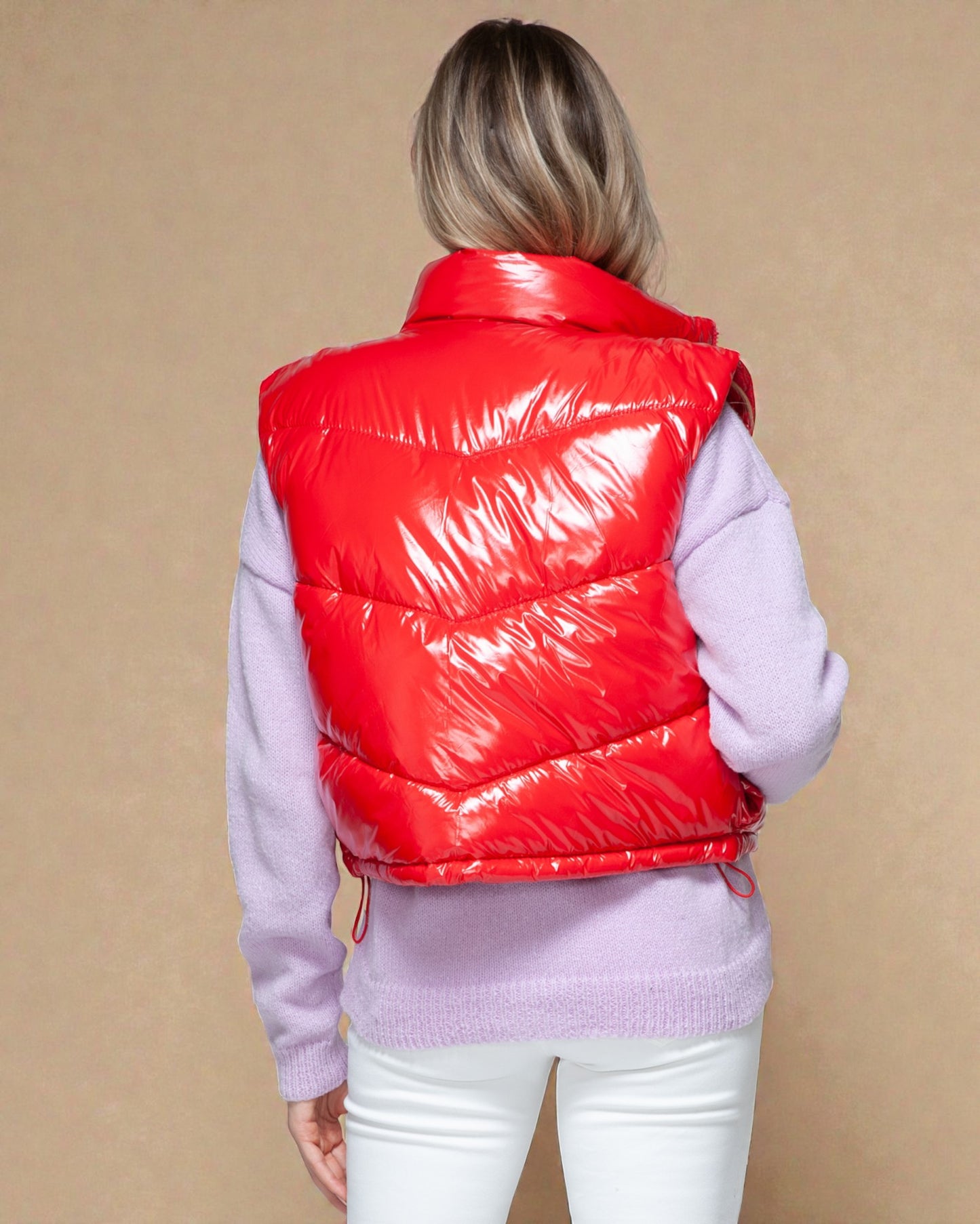 Person wearing a red puffer vest over a light purple sweater on a beige background