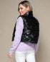 Woman wearing a black puffer vest over a light purple sweater on a beige background