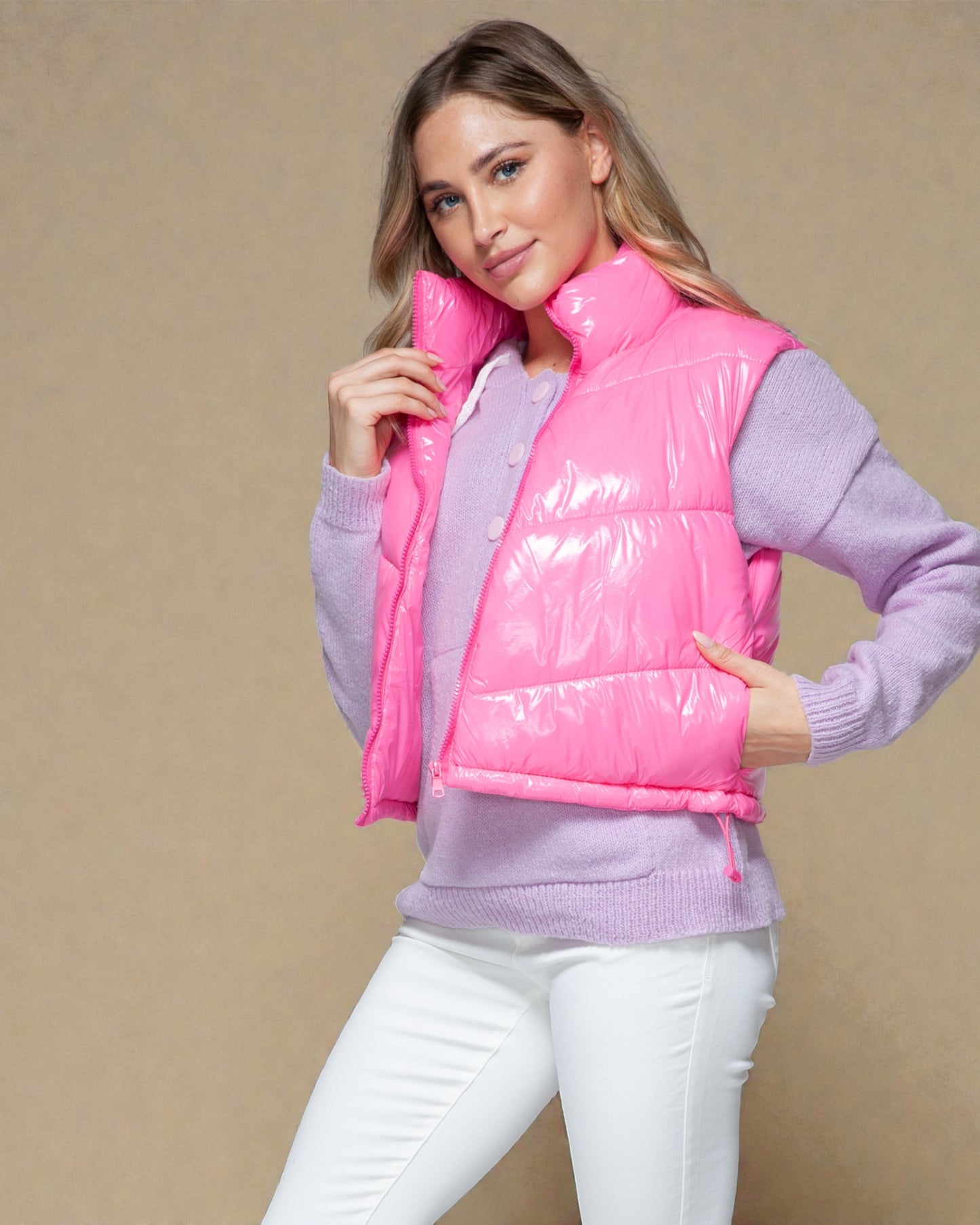 Woman wearing a pink puffer vest over a light purple sweater on a beige background