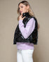 Woman wearing a black puffer vest over a purple sweater on a beige background