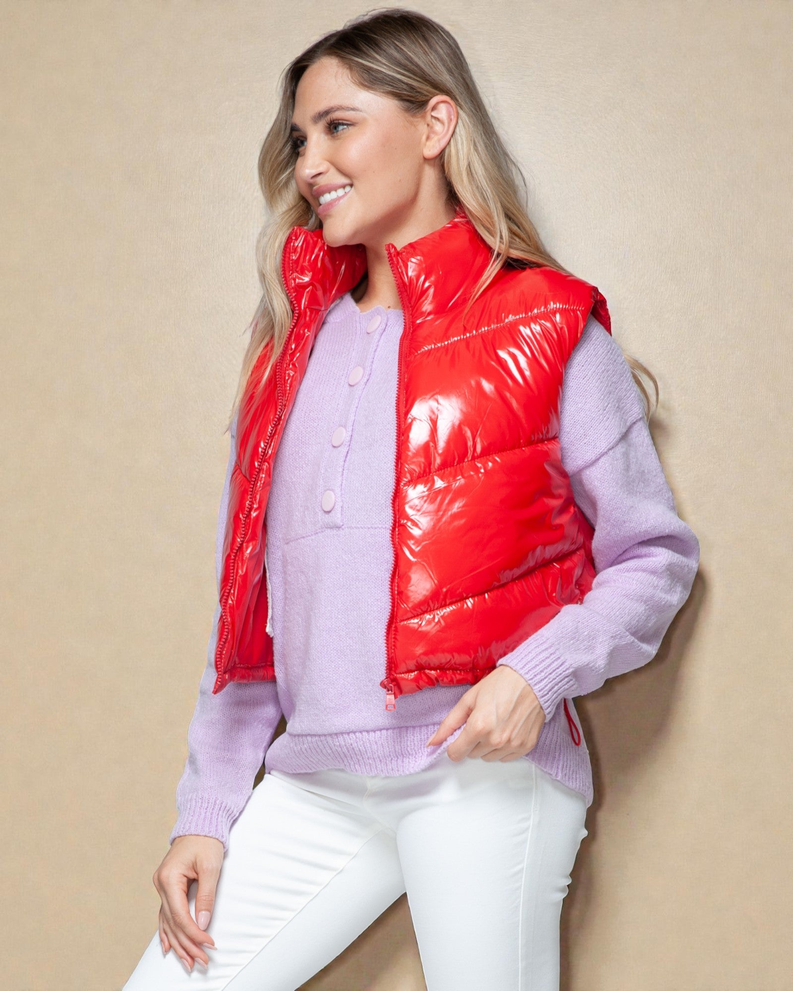 Woman wearing a red puffer vest over a light purple sweater against a beige background