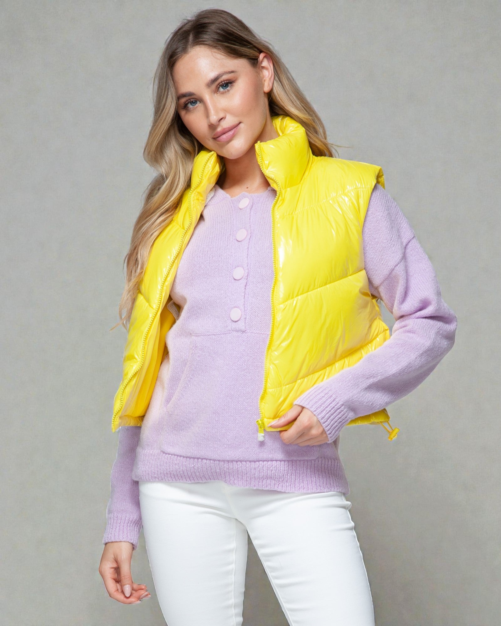 Woman wearing a yellow puffer vest over a purple sweater on a gray background