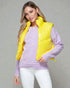 Woman wearing a yellow puffer vest over a purple sweater on a gray background