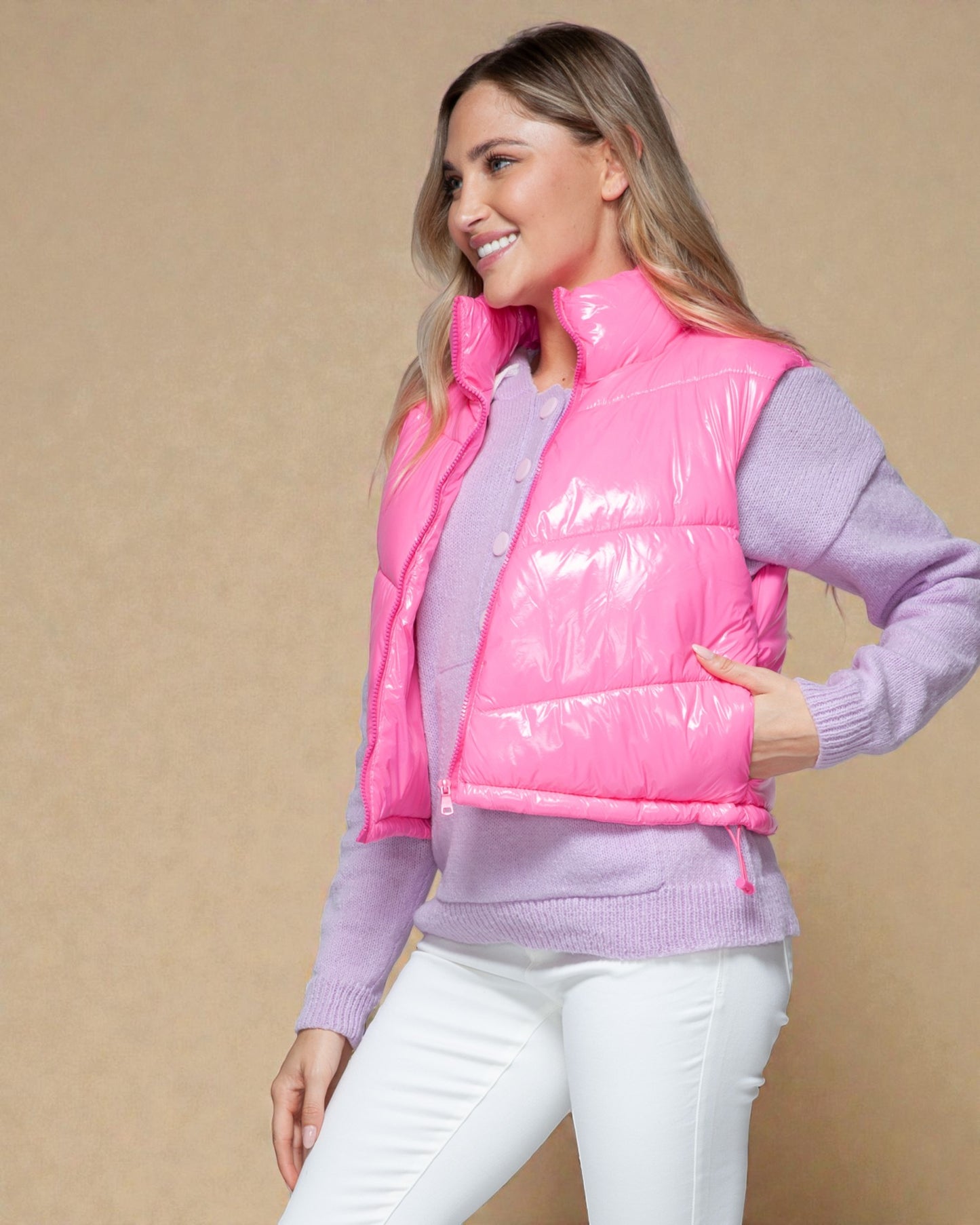 Woman wearing a pink puffer vest over a purple sweater on a beige background