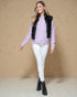 Woman wearing a lavender sweater, black puffer vest, white pants, and black boots against a beige background
