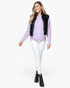 A woman modeling a lavender knit sweater vest with a glossy black patent leather trim, styled with white skinny jeans, black lace-up ankle boots, and a light purple button-up henley shirt against a plain white background.