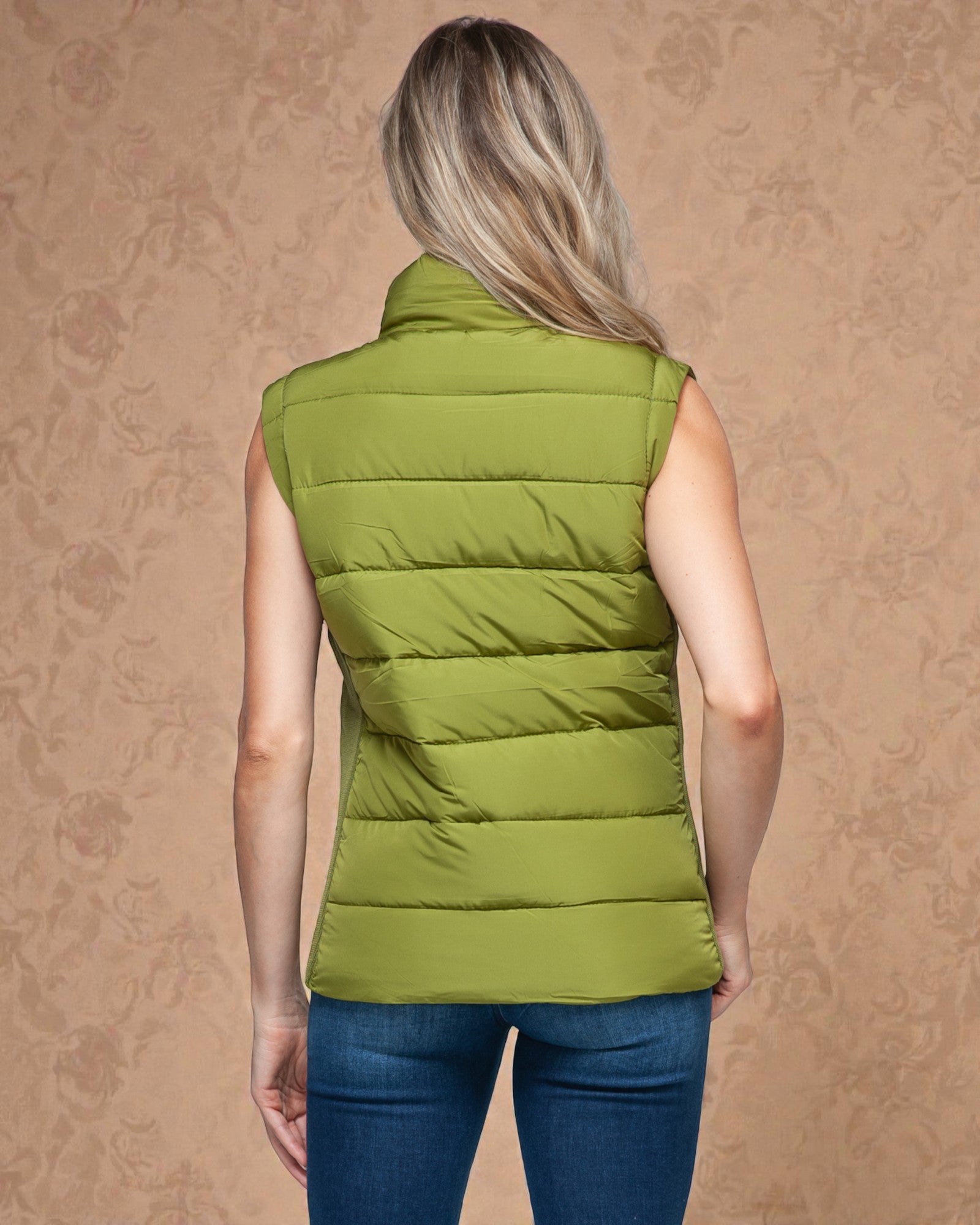 Person wearing a green puffer vest on a beige background