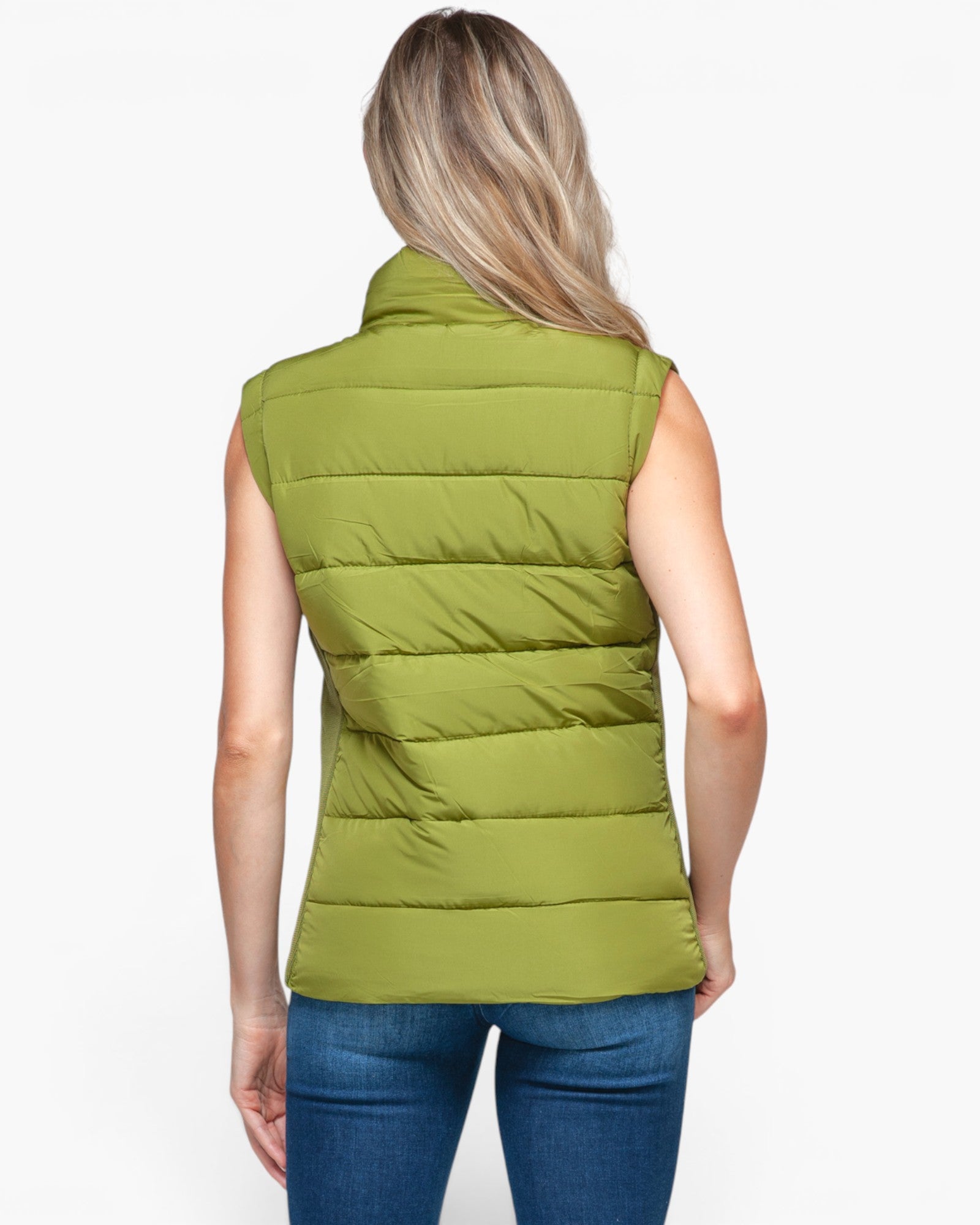 A woman viewed from the back wearing a sleeveless, quilted puffer vest in olive green, paired with blue jeans, against a plain white background.