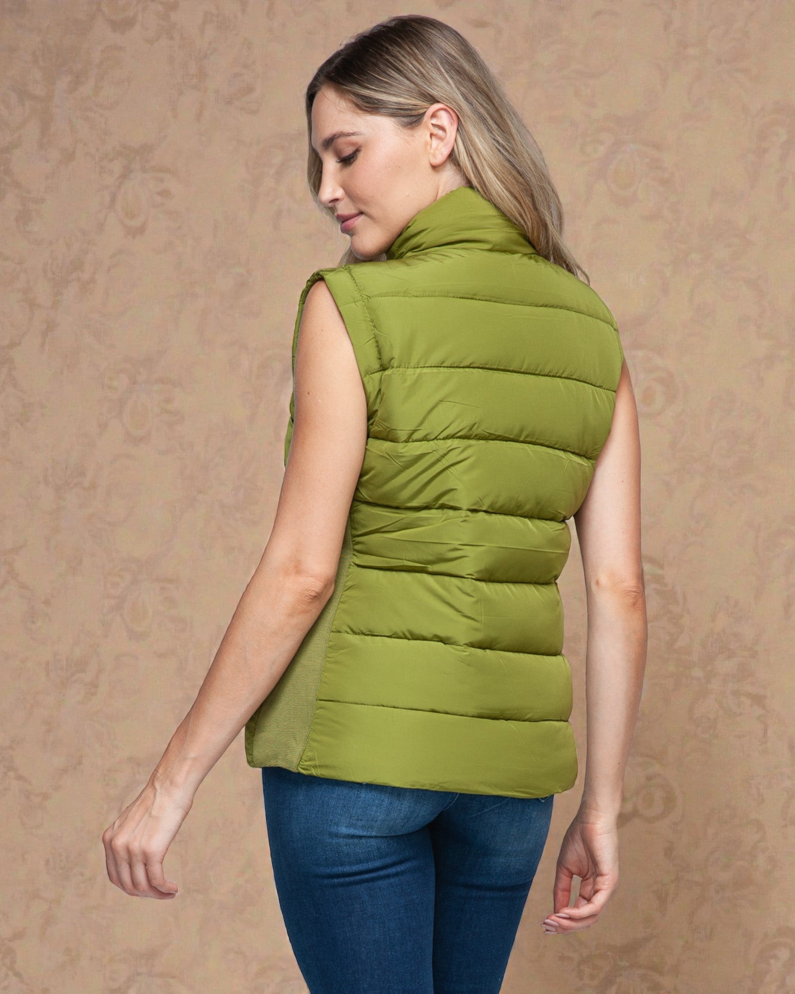 Woman wearing a green puffer vest against a beige background