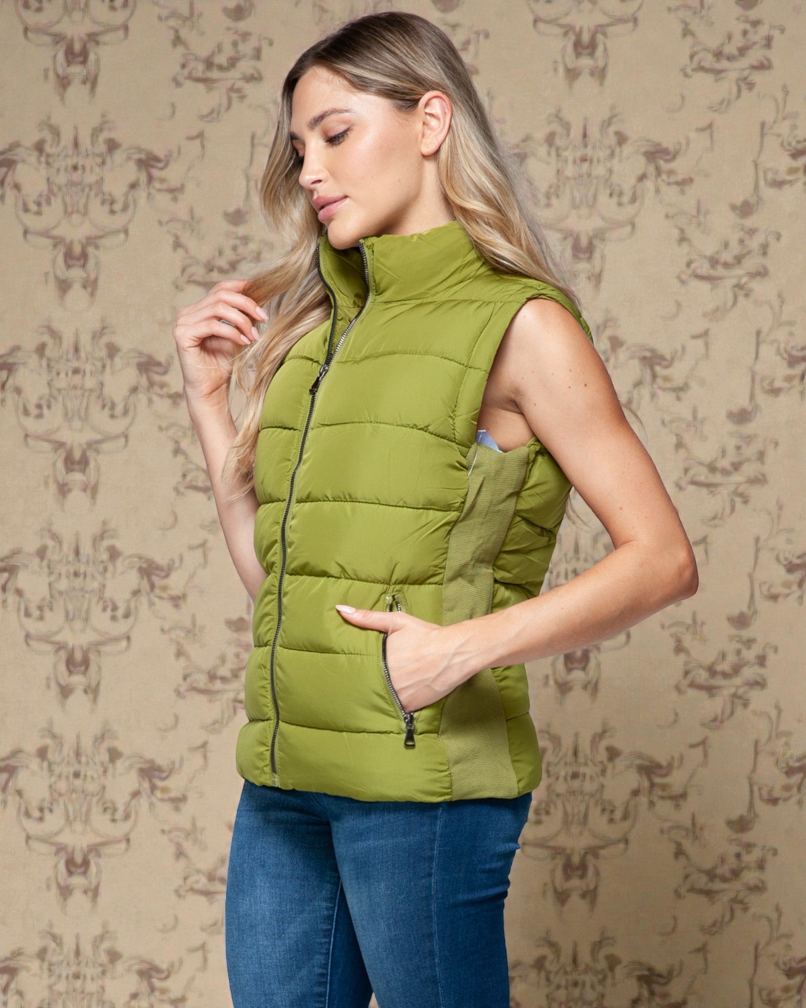 Woman wearing a green puffer vest against a patterned wall.