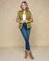 Woman wearing a green puffer vest, white shirt, blue jeans, and brown boots on a beige background