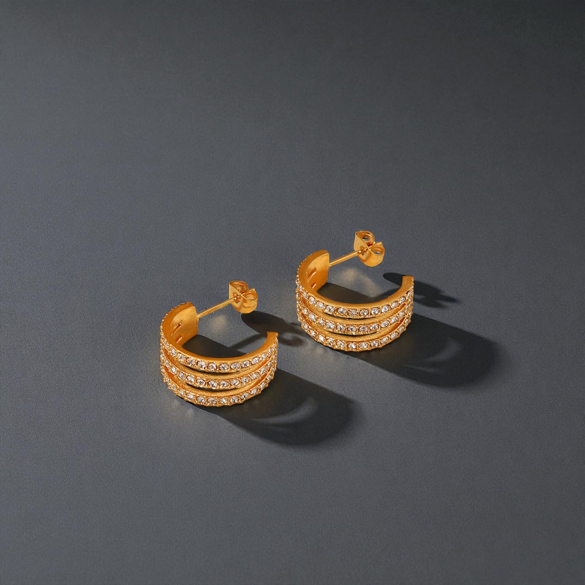 Pair of gold hoop earrings with clear stones on a dark gray background