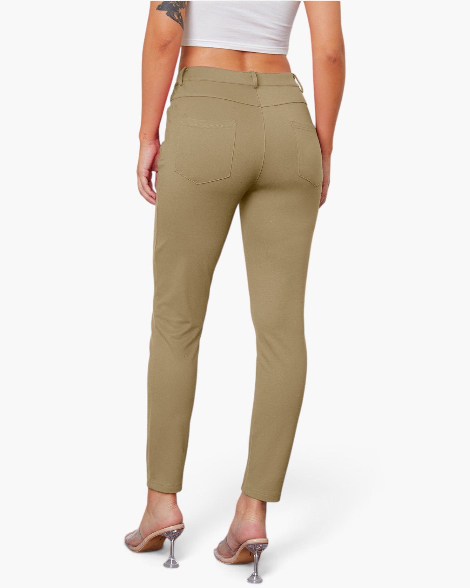A model shown from the back wearing slim-fit, high-waisted khaki pants with a button closure and back pockets, paired with a white crop top and clear high-heeled sandals.