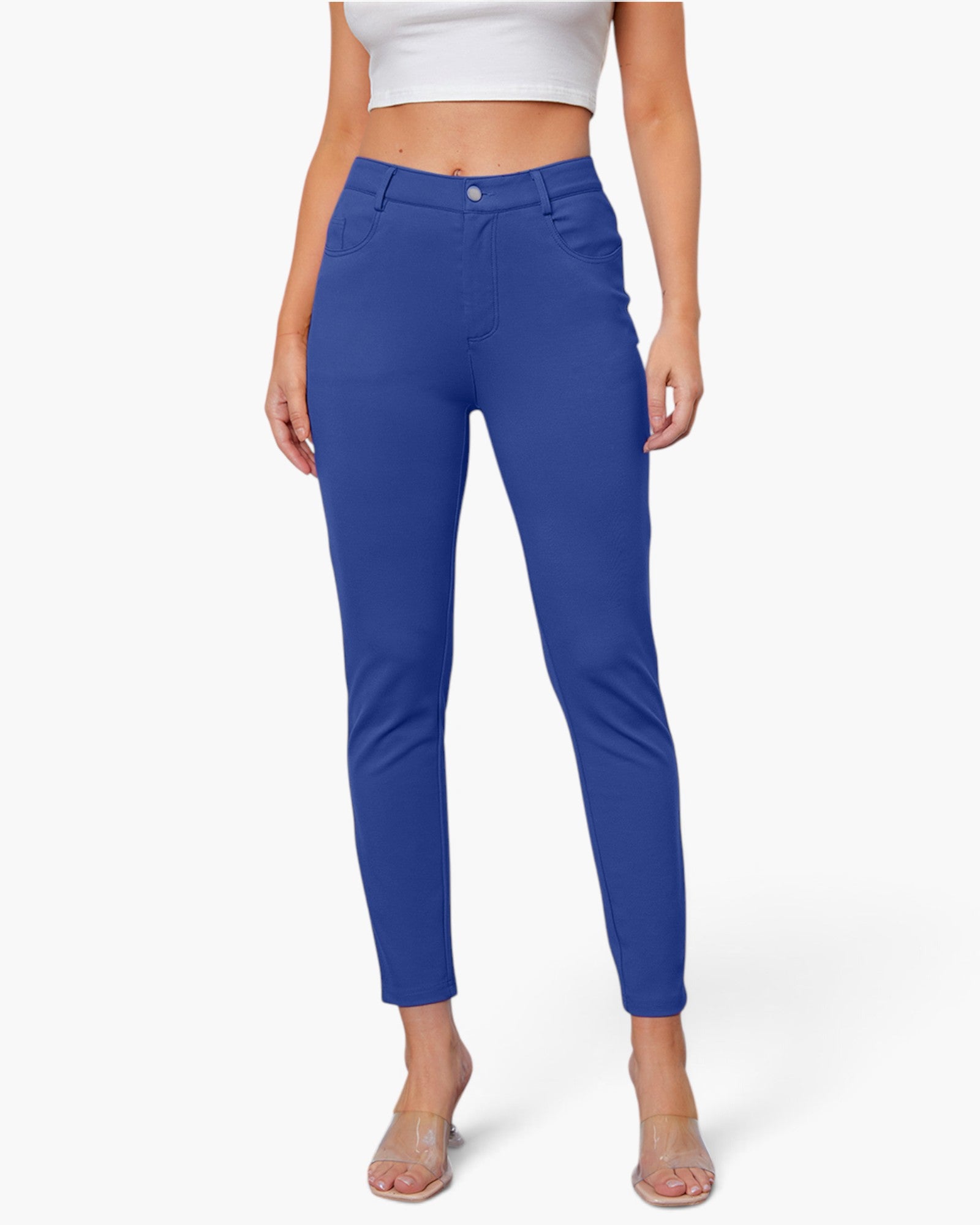 A model wearing a pair of royal blue slim-fit ankle-length pants, paired with a white crop top and clear high-heeled sandals, against a plain white background.