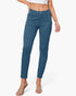 A model wearing a pair of slim-fit, ankle-length blue jeans with a white crop top and clear heeled sandals, shown from the waist down against a light gray studio background.