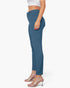 A side-profile view of a model wearing high-waisted, slim-fit blue pants with a white crop top and clear high-heeled mule sandals against a plain white background.