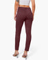 Rear view of a model wearing high-waisted, slim-fit burgundy pants with a button closure and back pockets, paired with a white crop top and clear high-heel mules, against a light gray studio background.