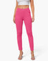 A model wearing bright pink slim-fit ankle-length pants with a white crop top and clear high-heeled sandals, shown against a light gray studio background.
