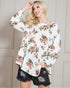 Woman wearing a floral blouse and black shorts against a neutral background