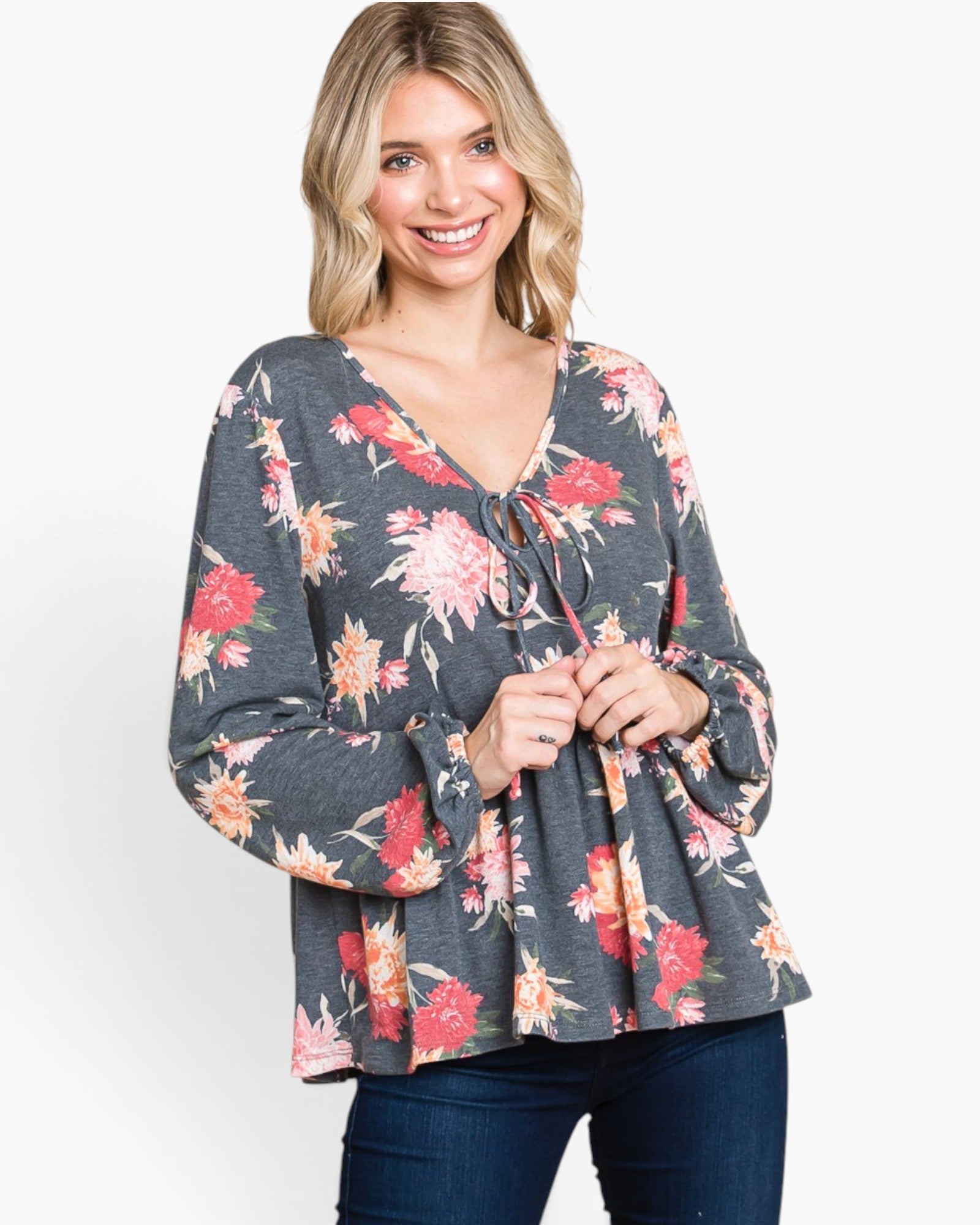 A woman wearing a dark gray long-sleeve blouse with a vibrant red, pink, and orange floral print, paired with dark blue jeans, against a plain white studio background.