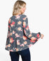 A woman shown from the back wearing a dark gray long-sleeve blouse with a pink, red, and peach floral print, paired with dark blue jeans, against a plain white background.
