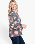 A woman modeling a dark gray long-sleeve blouse with a vibrant red, orange, and pink floral print, paired with dark blue jeans, against a plain white studio background.