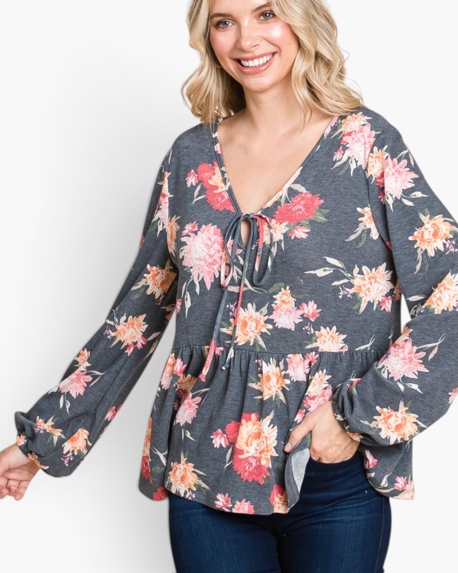 A woman wearing a dark gray long-sleeve blouse with a vibrant pink, red, and orange floral print, paired with dark blue jeans, against a plain white background.