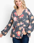 A woman wearing a dark gray long-sleeve blouse with a vibrant pink, red, and orange floral print, paired with dark blue jeans, against a plain white background.